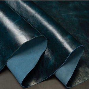 May include: Close-up of a deep teal leather with a textured, distressed finish. The leather is folded over, revealing a lighter blue underside.
