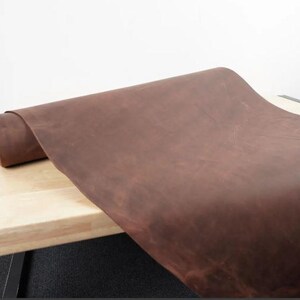 May include: A close-up of a brown leather sheet rolled up on a wooden surface. The leather has a natural, rustic look and feel.