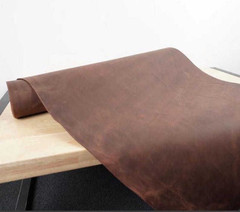 May include: A close-up of a brown leather sheet rolled up on a wooden surface. The leather has a natural, rustic look and feel.