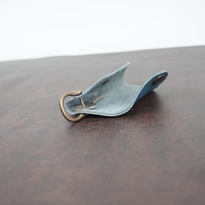 May include: A light blue leather key holder with a brass hook and a key inside. The holder is open and the key is visible.