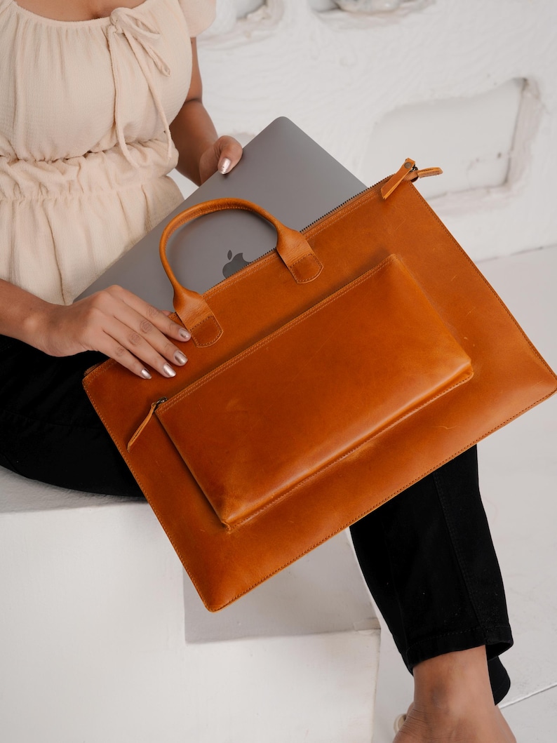 Op de afbeelding: Een set van drie bruine leren laptoptassen. De grootste tas heeft een ritssluiting en een rechthoekige vorm. De middelste tas is een kleinere rechthoekige pouch met een ritssluiting. De kleinste tas heeft een handvat.