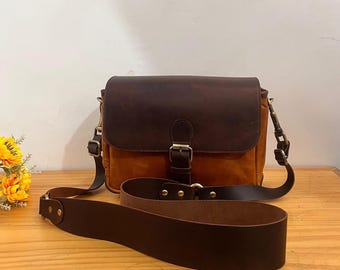 May include: A brown leather messenger bag with a flap closure and adjustable shoulder strap. The bag features a contrasting tan body and a dark brown leather flap secured with a brass buckle. An additional brown leather strap lies in front.