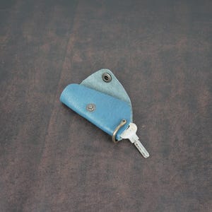 May include: A blue leather key holder with a metal ring and a key attached. The key holder is folded in half and has a flap that closes with a snap.