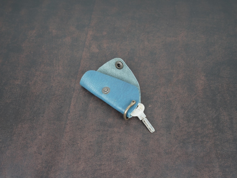 May include: A blue leather key holder with a metal ring and a key attached. The key holder is folded in half and has a flap that closes with a snap.