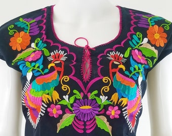 May include: Black embroidered cotton blouse with colorful floral and bird designs. The neckline has a pink tie closure.