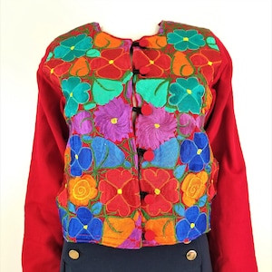 May include: A red embroidered jacket with colorful floral designs. The jacket has a button closure and long sleeves.
