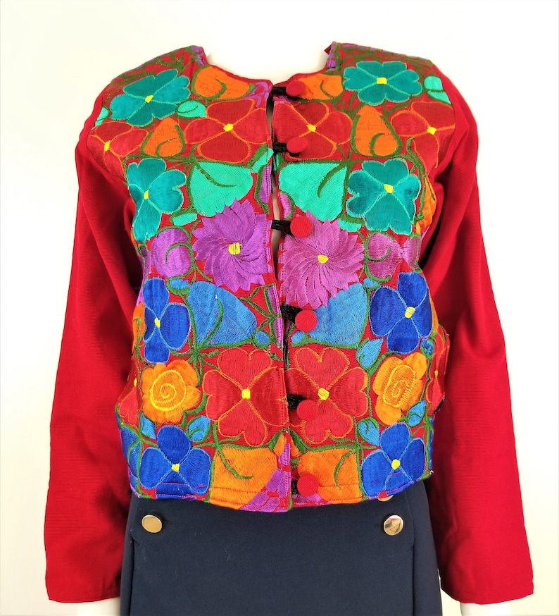 May include: A red embroidered jacket with colorful floral designs. The jacket has a button closure and long sleeves.