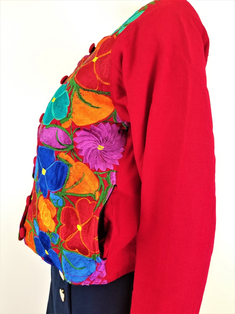May include: A red embroidered jacket with colorful floral designs. The jacket has a button closure and pockets.