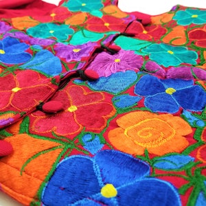 May include: A red embroidered blouse with colorful floral designs. The blouse has a button closure and is made of a soft, lightweight fabric.