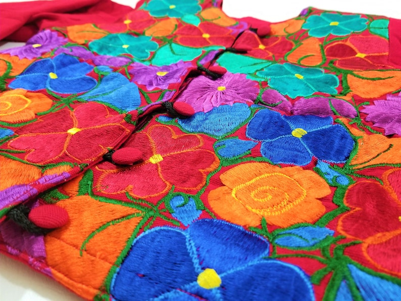 May include: A red embroidered blouse with colorful floral designs. The blouse has a button closure and is made of a soft, lightweight fabric.