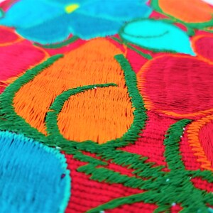May include: Close-up of a colorful embroidered fabric with red, orange, green, and blue thread. The fabric has a floral design with a repeating pattern.
