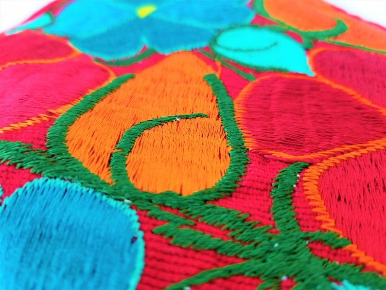 May include: Close-up of a colorful embroidered fabric with red, orange, green, and blue thread. The fabric has a floral design with a repeating pattern.