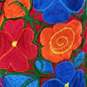 May include: Embroidered fabric with a floral design featuring red, orange, blue, and green flowers. The flowers are stitched with a raised texture.