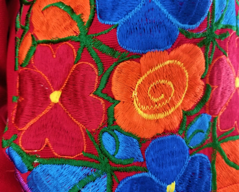 May include: Embroidered fabric with a floral design featuring red, orange, blue, and green flowers. The flowers are stitched with a raised texture.