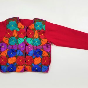 May include: A red embroidered jacket with a floral pattern in shades of blue, green, orange, purple, and red. The jacket has a button closure and long sleeves.
