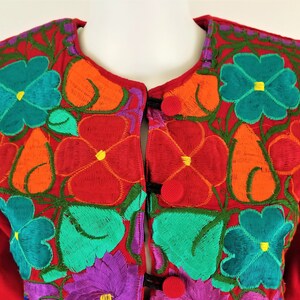 May include: Red cardigan with colorful floral embroidery. The embroidery features flowers in shades of orange, red, green, blue, and purple.