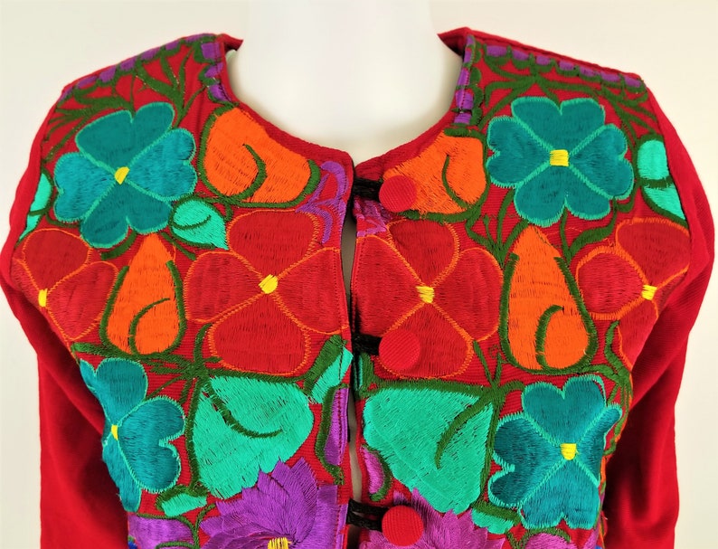 May include: Red cardigan with colorful floral embroidery. The embroidery features flowers in shades of orange, red, green, blue, and purple.