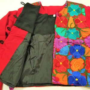 May include: A red jacket with a black lining and colorful floral embroidery. The jacket has a button closure and long sleeves.