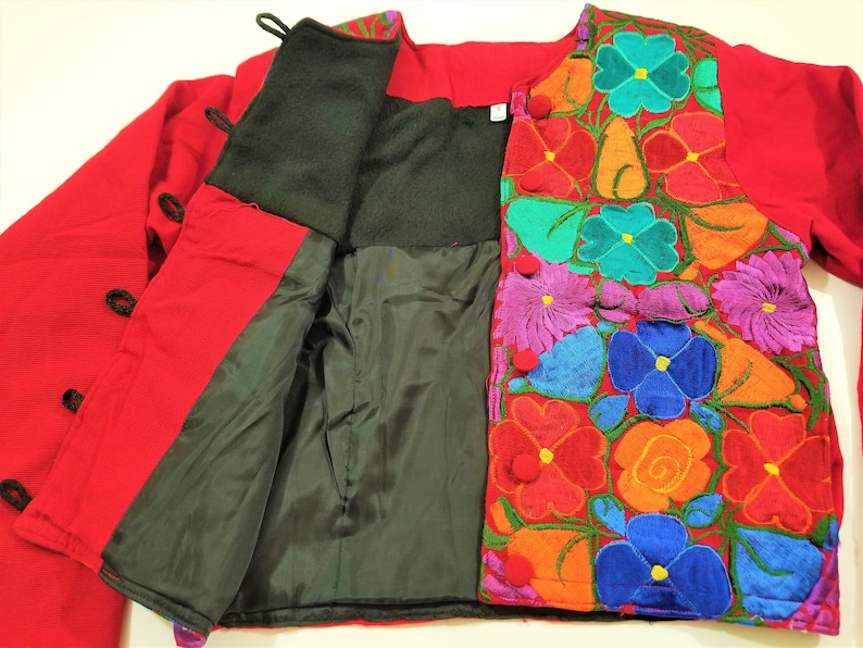 May include: A red jacket with a black lining and colorful floral embroidery. The jacket has a button closure and long sleeves.