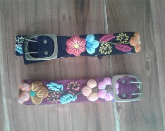 May include: Two embroidered belts with floral designs. The top belt is black with a silver buckle and the bottom belt is burgundy with a silver buckle.