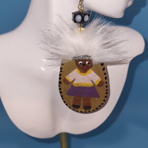 May include: Gold-toned dangle earrings. Each earring features a black bead with white accents, a white fluffy accent, and a hand-painted pendant depicting a figure in a purple skirt and yellow-trimmed shirt.