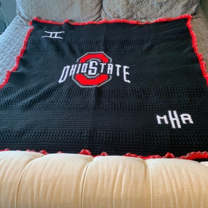May include: Black crochet blanket with a red border and white crocheted Ohio State logo in the center. The blanket also has the initials "MHA" in white crochet.