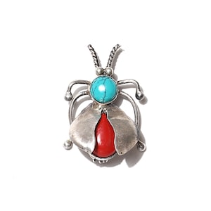 May include: A silver pendant in the shape of a beetle with a turquoise and red stone inlay.