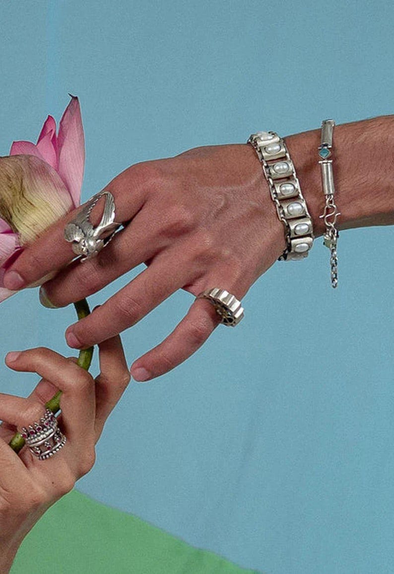 Puede incluir: Una pulsera de plata con incrustaciones ovaladas blancas, una pulsera de cadena fina de plata con una peque&ntilde;a piedra azul, un anillo de plata con dise&ntilde;o de ala, un anillo de banda ancha y un anillo de plata con piedras rosas.