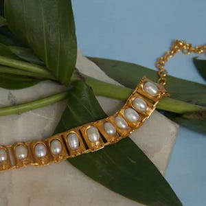 Puede incluir: Una pulsera de tono dorado que presenta una serie de eslabones rectangulares, cada uno engastado con una perla blanca ovalada. La pulsera incluye una delicada cadena de extensi&oacute;n dorada con eslabones circulares para un ajuste regulable.