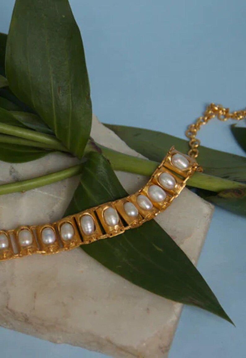 Puede incluir: Una pulsera de tono dorado que presenta una serie de eslabones rectangulares, cada uno engastado con una perla blanca ovalada. La pulsera incluye una delicada cadena de extensi&oacute;n dorada con eslabones circulares para un ajuste regulable.