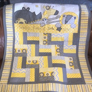 May include: A yellow and gray baby quilt with a patchwork design. The quilt features a variety of animal appliques, including a giraffe, a crocodile, and a bear. The quilt is bordered with a yellow and gray striped fabric. The text "Twinkle Twinkle Little Star" is printed on the quilt.
