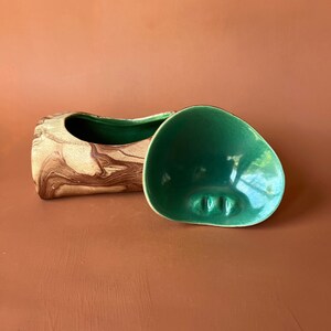 May include: A ceramic planter shaped like a log with a green lid. The planter has a brown and white marbled design.