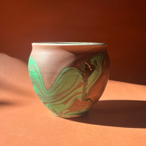 May include: A small, round ceramic pot with a brown and green marbled glaze. The pot is perfect for displaying small plants or succulents.