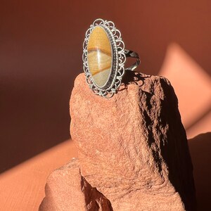 Op de afbeelding: Een zilveren ring met een ovale steen gezet in een filigraan ontwerp. De steen is een gebandeerde agaat met bruine, witte en gele strepen.