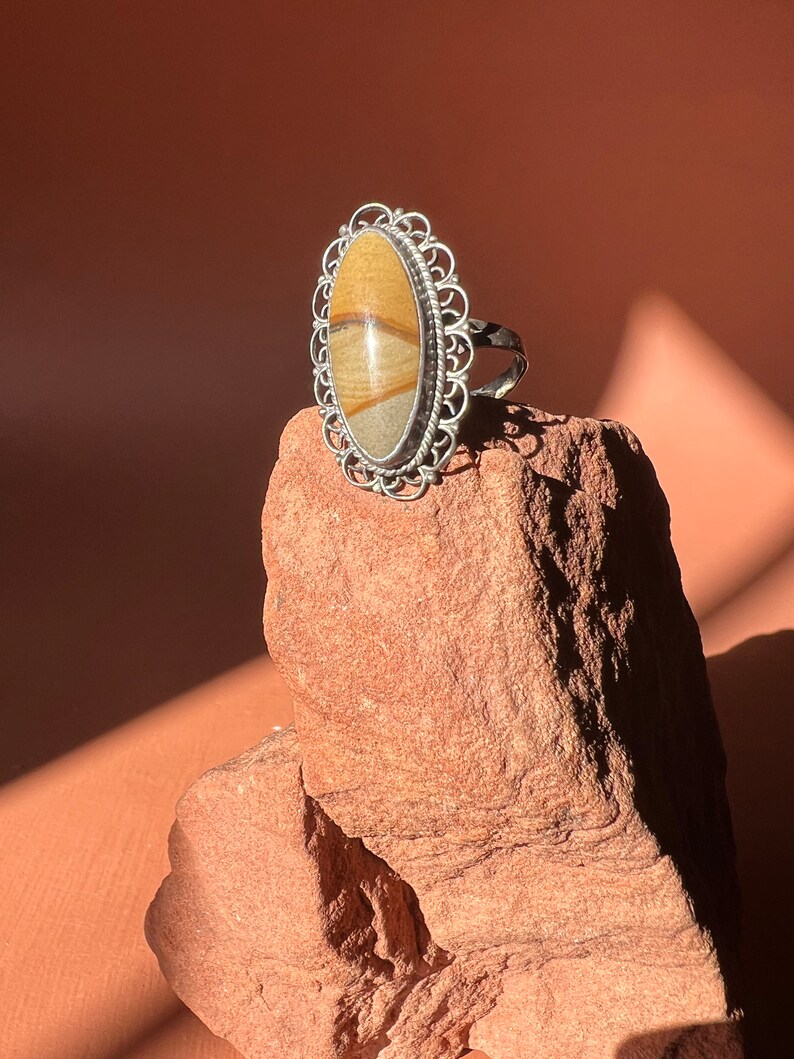 Op de afbeelding: Een zilveren ring met een ovale steen gezet in een filigraan ontwerp. De steen is een gebandeerde agaat met bruine, witte en gele strepen.