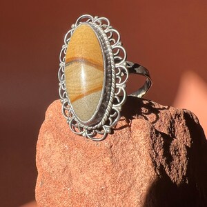 Op de afbeelding: Een zilveren ring met een grote ovale steen gezet in een filigraan ontwerp. De steen is lichtbruin met donkerbruine strepen.