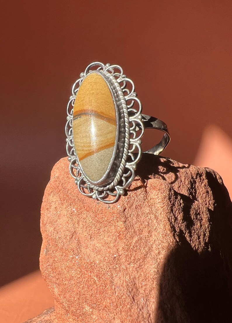 Op de afbeelding: Een zilveren ring met een grote ovale steen gezet in een filigraan ontwerp. De steen is lichtbruin met donkerbruine strepen.