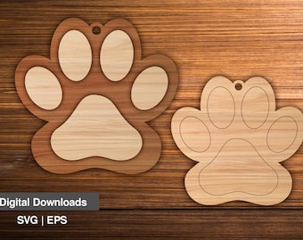 May include: Two wooden paw print ornaments, one larger than the other, with a hole at the top for hanging. The ornaments are on a woodgrain background.