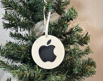 May include: White round Christmas ornament with a black Apple logo. The ornament is hanging on a green artificial Christmas tree.