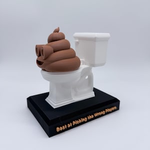 Puede incluir: Una figura humorística que presenta un emoji de caca marrón sonriente sentado en un inodoro blanco. La base negra tiene el texto "Best at Picking the Wrong Players".