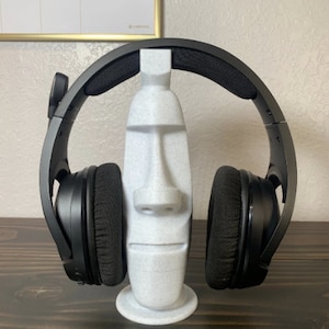 May include: A white 3D printed head stand with a textured surface, holding a pair of black headphones.