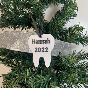 May include: White tooth-shaped Christmas ornament with the name "Hannah" and the year "2022" written in black.