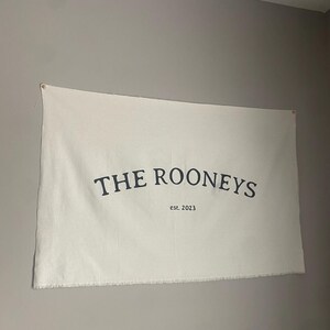 May include: A white canvas banner with black text that reads "THE ROONEYS est. 2023".