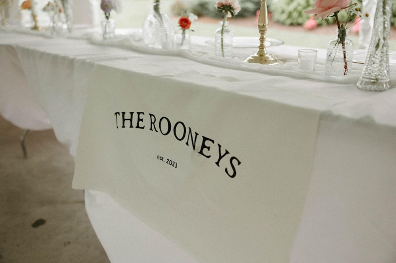 May include: White table runner with black text that reads "THE ROONEYS est. 2023".