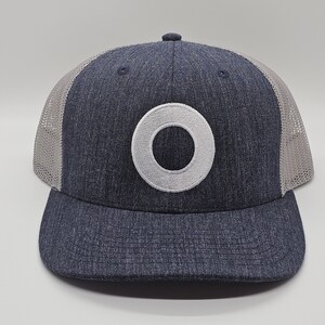 May include: A navy blue and gray trucker hat with a white embroidered circle on the front.
