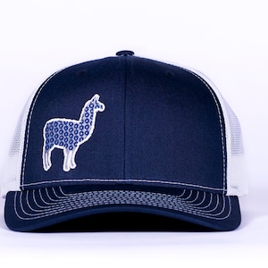 Könnte beinhalten: Eine marineblaue und weiße Trucker-Kappe mit einem gestickten Lama in blau-weißem Muster auf der Vorderseite.