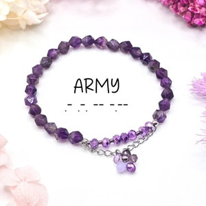 May include: Purple amethyst gemstone bracelet with a charm of smaller purple and lavender gemstones hanging from a silver chain. The bracelet has the word "ARMY" written in black text and a line of dashes below it.