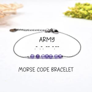 May include: A delicate silver-toned bracelet featuring a series of small, faceted purple beads. The word "ARMY" is displayed above the Morse code representation. The text "MORSE CODE BRACELET" is printed below the bracelet.