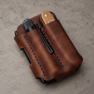 May include: A brown leather pocket organizer featuring two vertical slots. One slot holds a black metal pen with a pocket clip, while the other slot contains a small folding pocket knife with a textured gold-colored handle and a silver rivet.