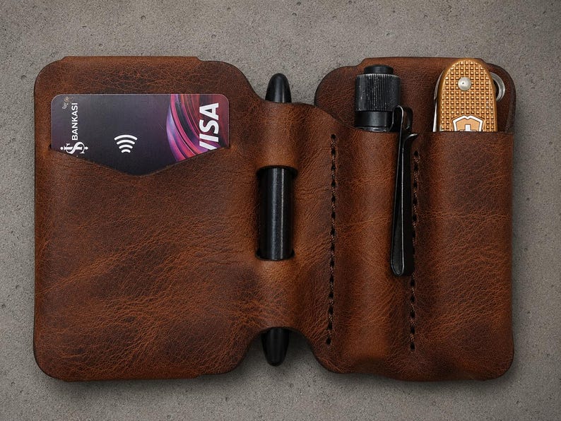 May include: A brown leather pocket organizer featuring a dedicated slot for a credit card, a central loop holding a black pen, and two additional vertical sleeves containing a small black flashlight and a gold-colored folding pocket knife.